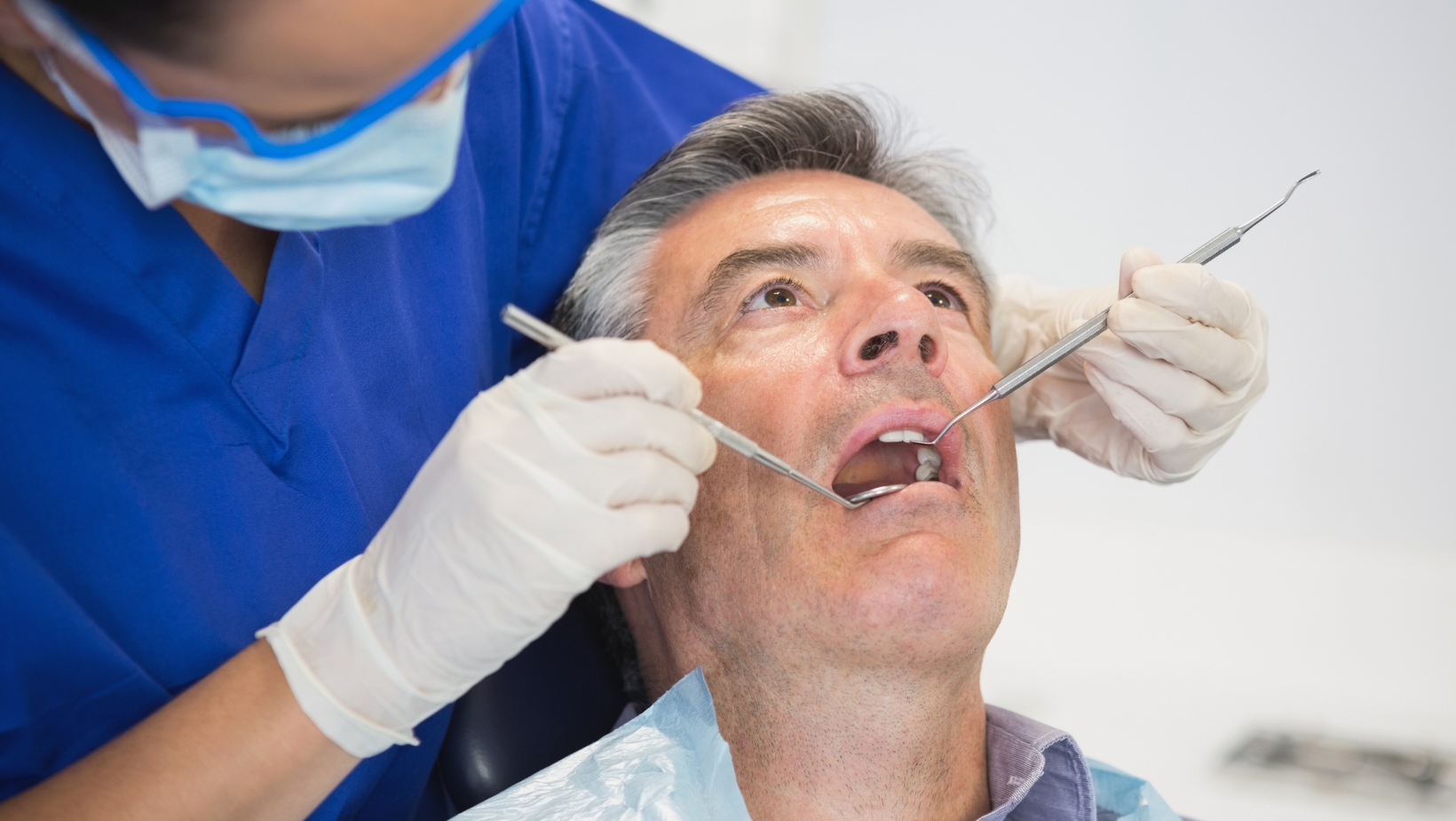 dentist examining patient teeth during dental checkup with dental tools